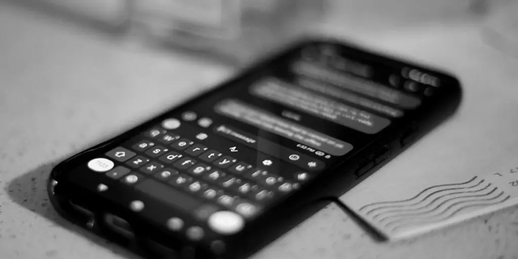 A black and white photo of a phone on a letter. The phone shows a blurred text exchange, with the last message read receipt showing unread by displaying an empty checkmark.